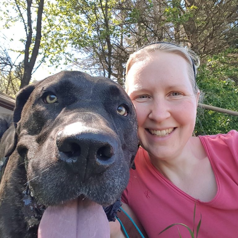 Eine junge Frau lächelt im Rahmen eines Selfies mit ihrem Hund in die Kamera.